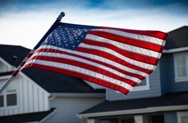 service-1 A close-up of the American flag waving in front of a suburban house, symbolizing patriotism.